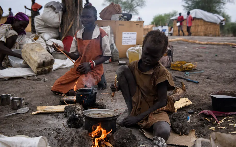 Viele der Kinder leiden bereits unter Mangelernährung | © UNICEF/Hatcher-Moore Südsudan: Ein Kind sitzt neben einem Kochtopf am Feuer