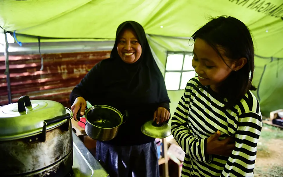Sophia und ihre Mutter bei den Essensvorbereitungen im Hilfszelt. | © UNICEF/UN0251769/Wilander Sulawesi: Sophia und ihre Mutter bereiten das Essen an einer Kochstelle vor.