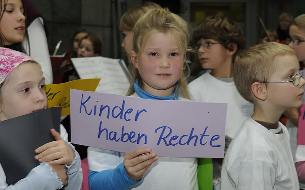 Ein Mädchen hält ein Schild hoch mit der Aufschrift: "Kinder haben Rechte".