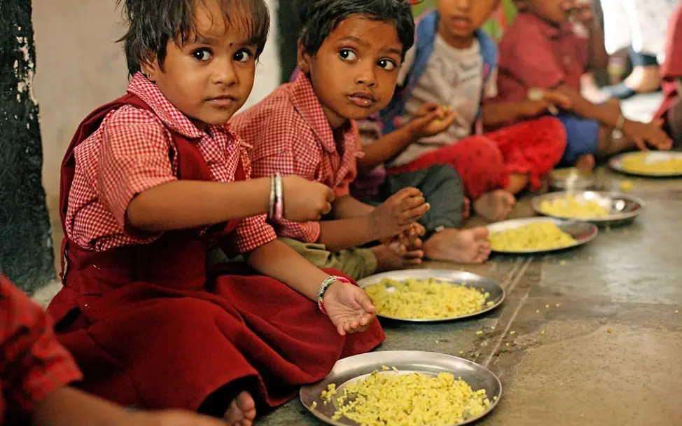 Im Dorf Sisarma in Indien essen Kinder zu Mittag. | © UNICEF/Kolari Kinder sitzen in einer Reihe und essen Reis von ihren Tellern.