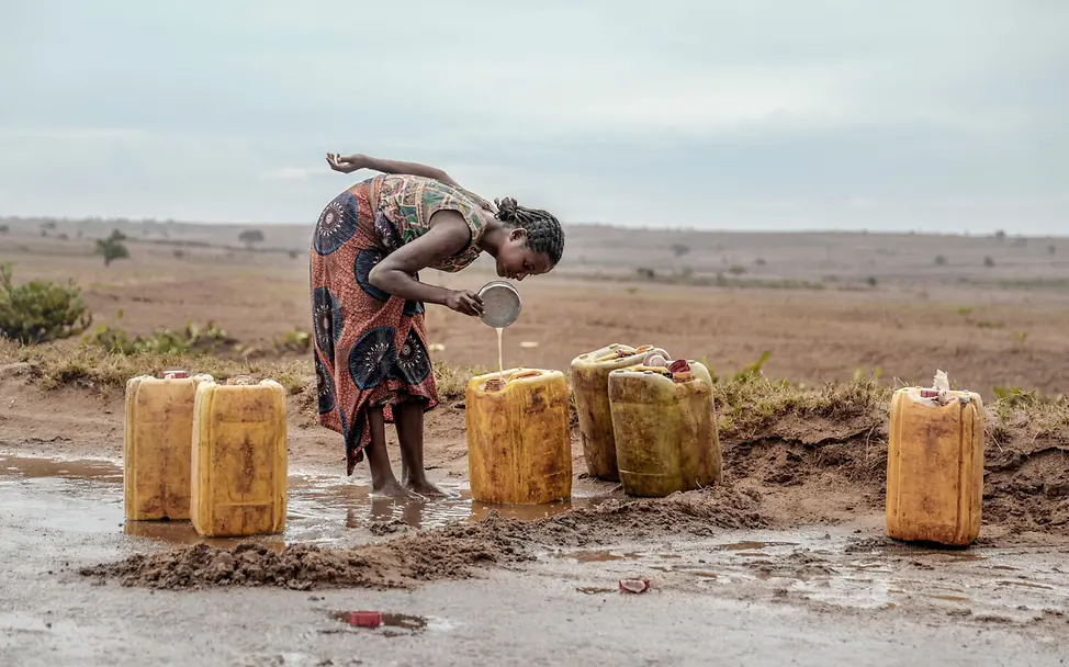 Eine Frau schöpft Regenwasser von der Straße in ihre Wasserkanister. © UNICEF/UN0406739/Andriananten UN0406739