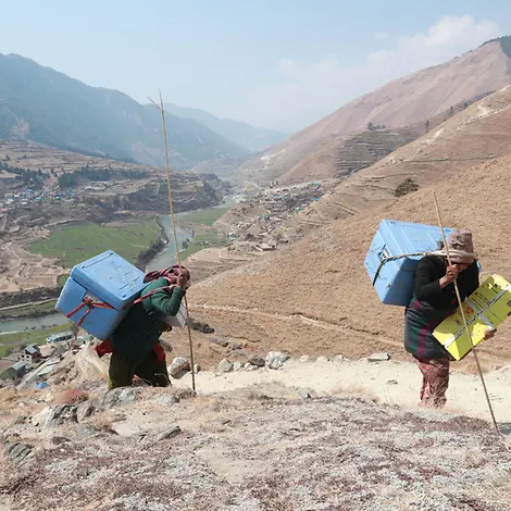 Covid-Vakzine erreichen Nepals entlegenste Region. | © UNICEF/UN0431115/ Zwei Gesundheitshelfer tragen den Covid-19-Impfstoff auf ihrem Rücken den Berg hoch.