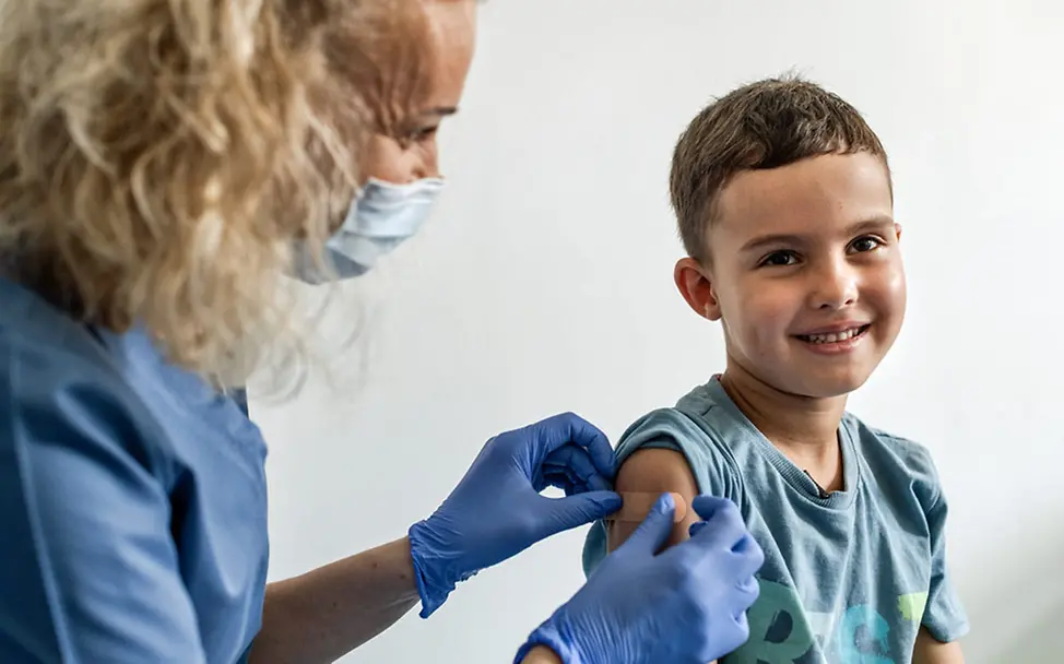 Ein Junge lächelt, während eine Gesundheitshelferin ihm ein Pflaster auf den Arm klebt. | © UNICEF/Strek Impfungen Baby: Bei Windpocken gibt es auch schwere Krankheitsverläufe.