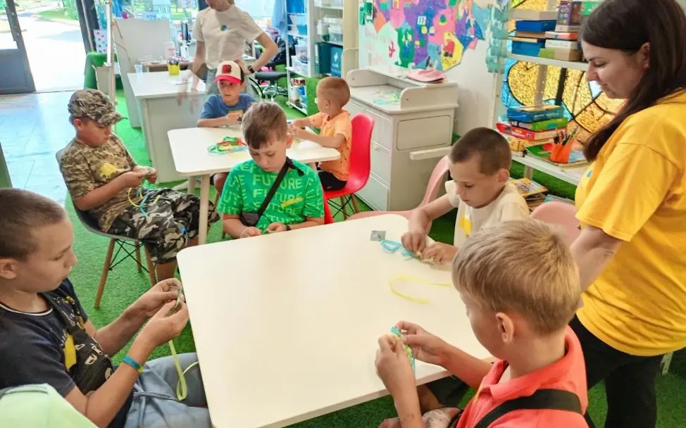 Ukraine: Kinder nehmen an Workshop teil |© UNICEF/unknown Jahrestag Ukraine-Krieg: Kinder sitzen an einem Tisch und basteln Armbänder.