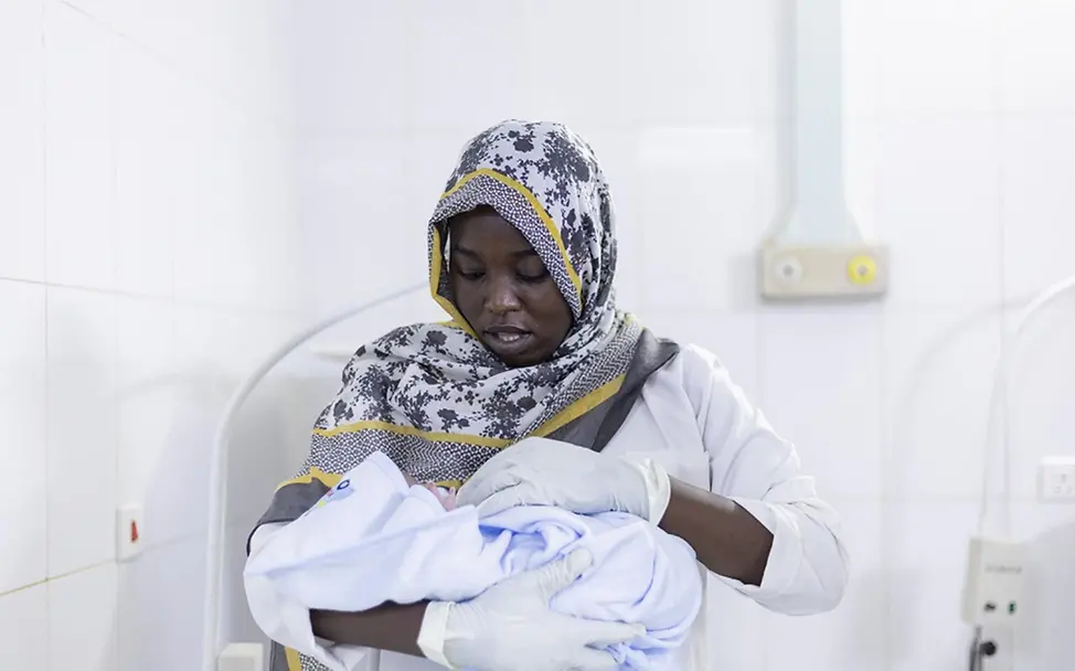 Hebamme Narameg bei der Arbeit | UNICEF/Mohamdeen Sudan Hungersnot: Hebamme Narameg hält ein Kind im Arm