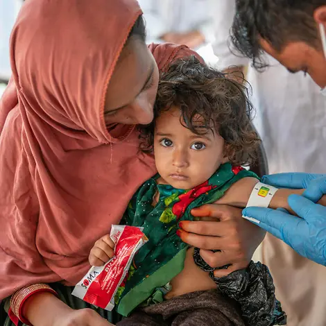 Zarmina mit einer Packung Erdnusspaste | © UNICEF/UNI403547/Karimi Ein Kind wird untersucht und erhält Erdnusspaste