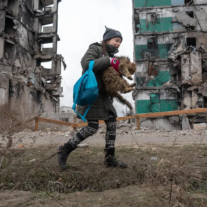 Die junge Veronica besucht ihr zerbombtes Zuhause | © UNICEF/UN0780449/Filippov Ein junges Mädchen mit einer Katze im Arm vor ihrem ehemaligen, nun zerbombten Zuhause