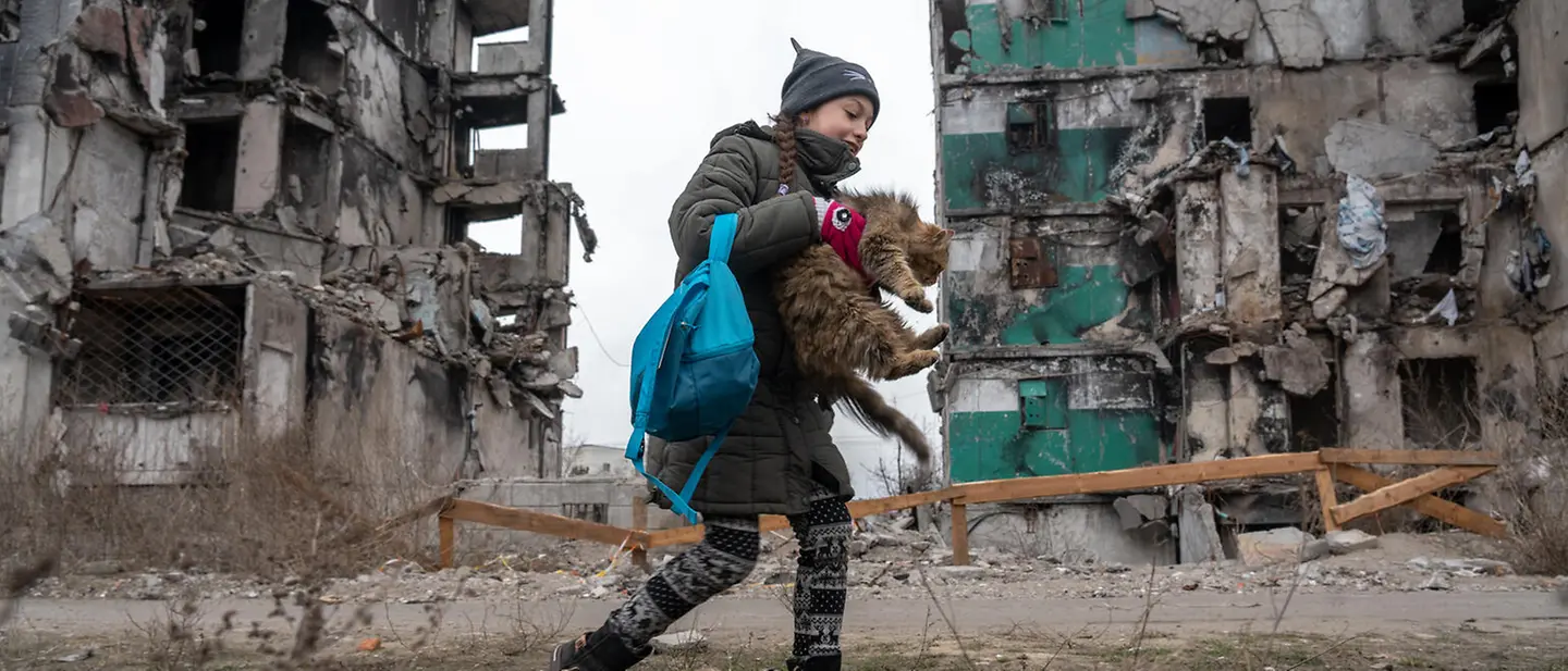Die junge Veronica besucht ihr zerbombtes Zuhause | © UNICEF/UN0780449/Filippov Ein junges Mädchen mit einer Katze im Arm vor ihrem ehemaligen, nun zerbombten Zuhause