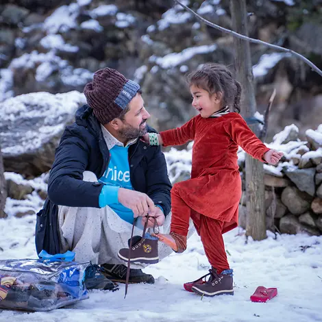 Humanitäre Hilfe im Jahr 2024 | © UNICEF/UN0779309/Khan Ein Helfer von UNICEF hilft einem kleinen Kind in einen Schuh