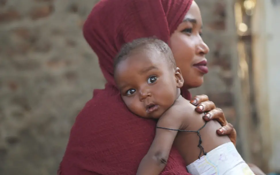 Eine Mutter hat ihr Kleinkind auf dem Arm welches in die Kamera schaut
