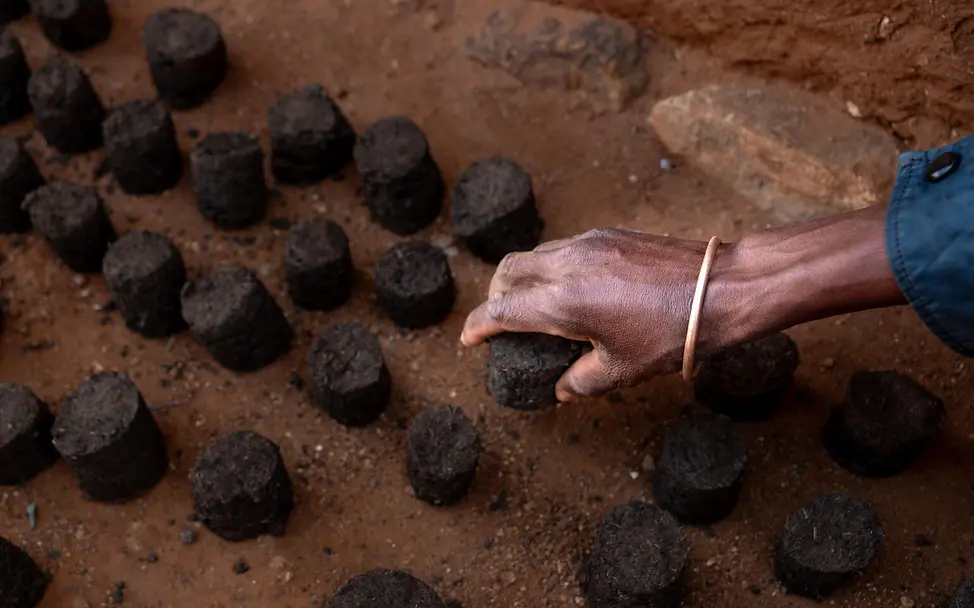 Ökologisch abbaubare Kohle im Ecovillage | © UNICEF/UNI658461/Andrianantenaina Eine Männerhand nimmt ein Stück ökologisch abbaubare Kohle in die Hand