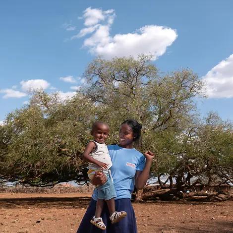 Annik und ihr Sohn | © UNICEF/UNI658499/Andrianantenaina Ein junges Mädchen steht mit ihrem Sohn auf dem Arm vor einem Baum