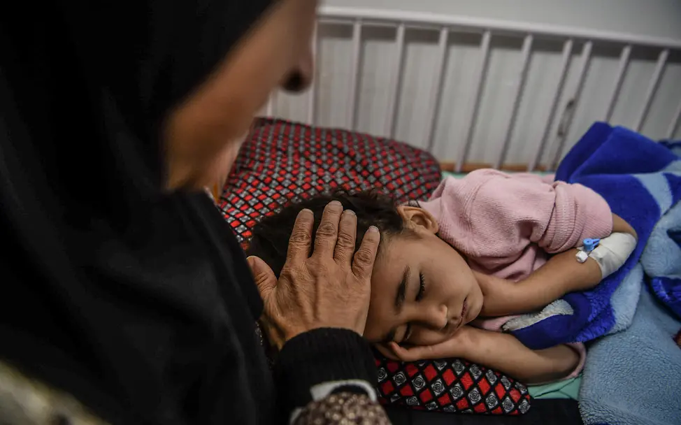 Ghazal im Krankenhaus | © UNICEF/UNI488710/Zaqout Ein kleines Mädchen schläft, eine Frau streichelt ihren Kopf