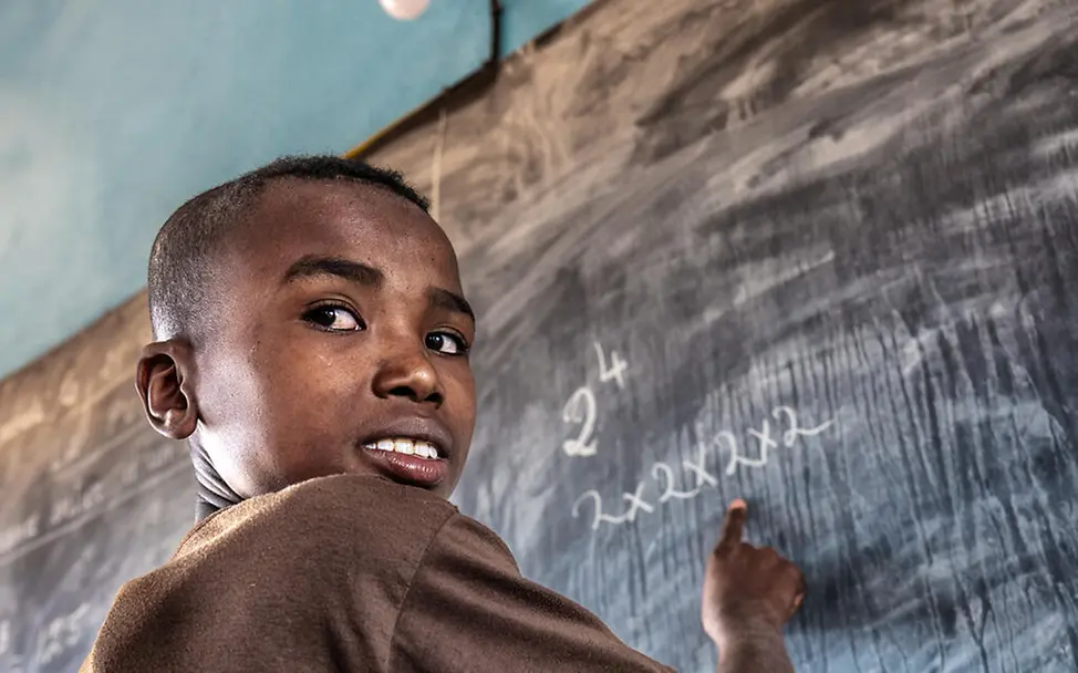 Zafia in der Schule |© UNICEF/UNI658435/Andrianantenaina Ein Junge steht an einer Tafel und schaut in die Kamera