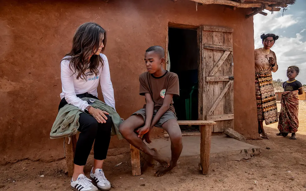 Zafia und Tessa Page | © UNICEF/UNI666724/Andrianantenaina Ein Junge und eine Frau sitzen auf einer Bank vor einem Haus