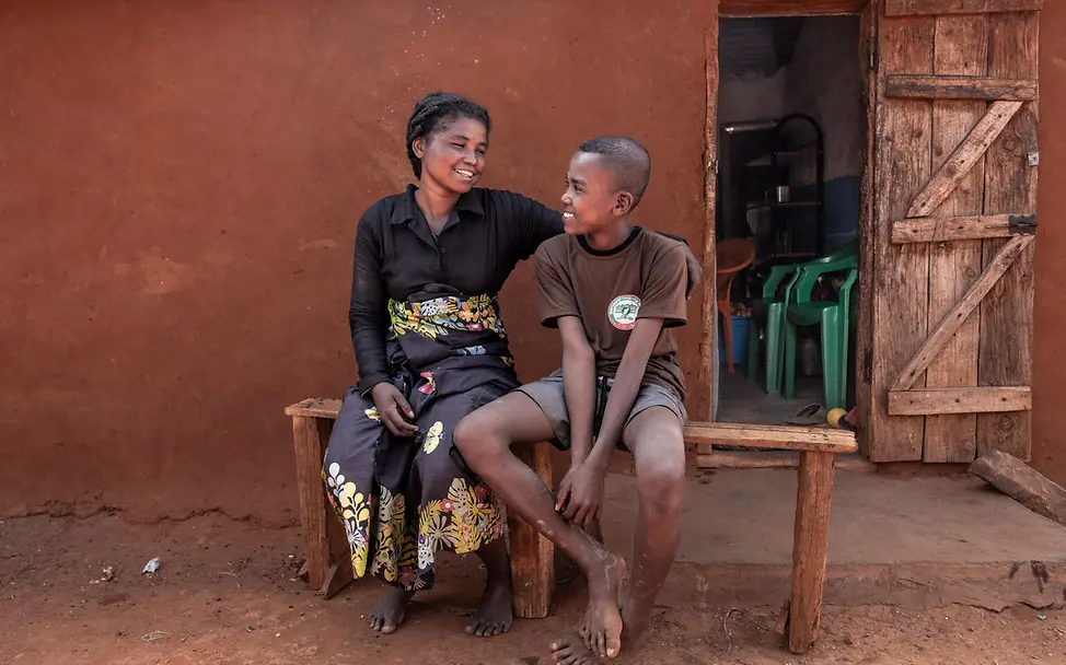 Zafia und seine Mutter | © UNICEF/UNI658439/Andrianantenaina Ein Junge sitzt mit einer Frau auf einer Holzbank