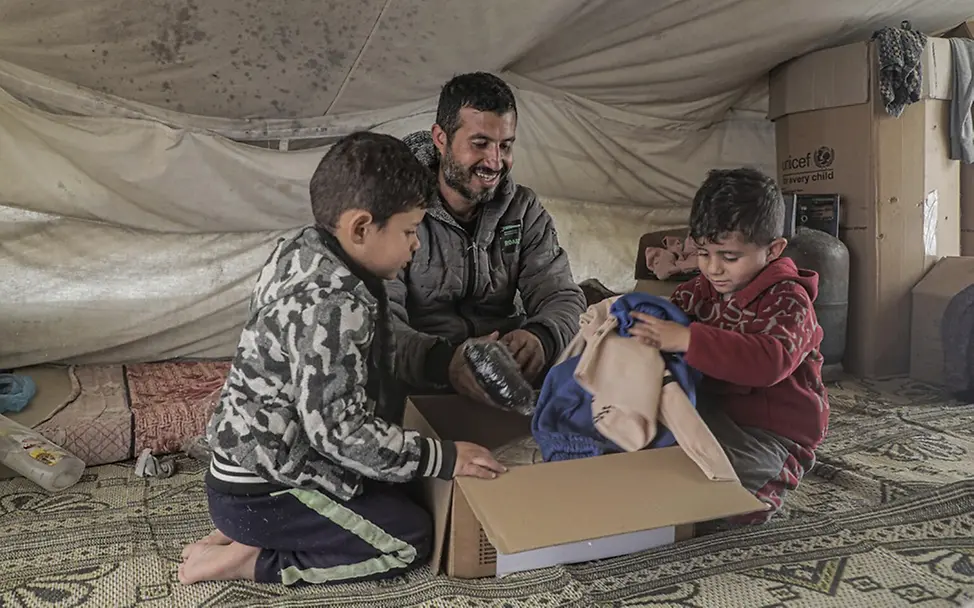 Eine Familie packt einen Karton mit warmer Kleidung aus | UNICEF/Nateel Gaza Waffenruhe: UNICEF verteilt Hilfsgüter