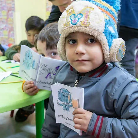 Ein kleines Kind hält ein gemaltes Bild in die Kamera