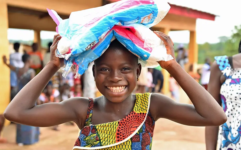 Ein Mädchen in der Elfenbeinküste trägt mehrere Päckchen Moskitonetze nach Hause.