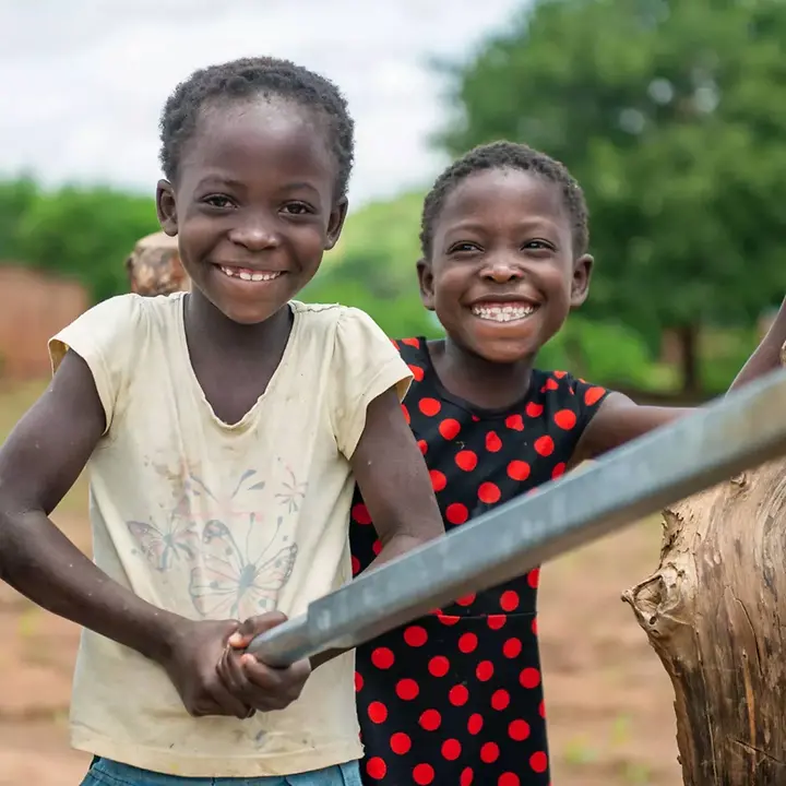 Zwei Mädchen in Sambia pumpen gemeinsam sauberes Trinkwasser aus einer Pumpe | © UNICEF/Sambia Sambia Wasser und Hygiene: Zwei Mädchen pumpen lächelnd Wasser