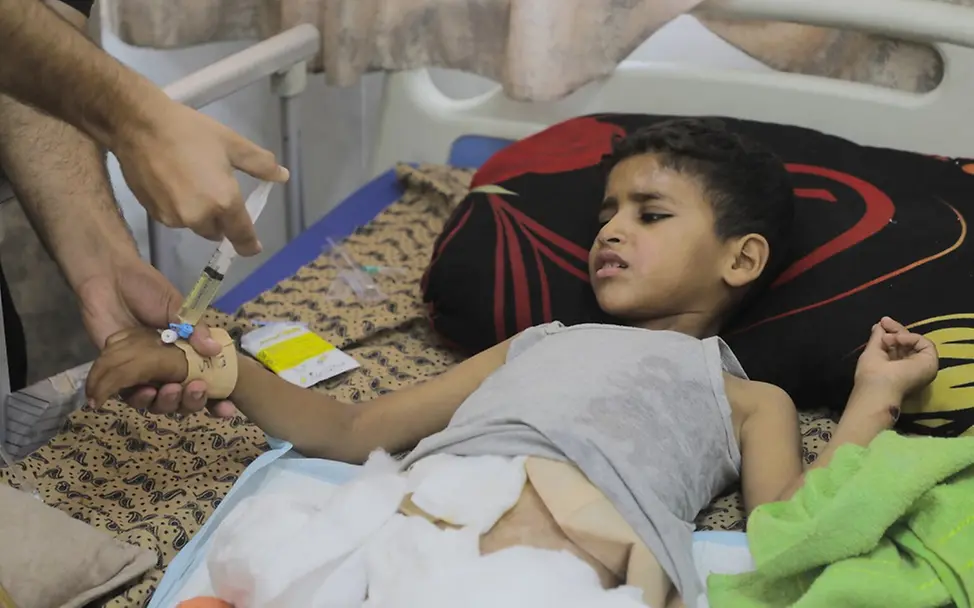 Sanad (10) nach der Amputation seines rechten Beins im Krankenhaus. | © UNICEF/Nateel Der zehnjährige Sanad liegt nach der Amputation seines rechten Beins in einem Krankenhausbett und bekommt eine Spritze.