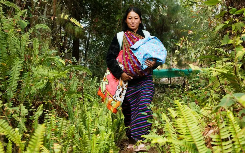 Eine junge Mutter auf dem Weg durch den Dschungel, um ihr Baby impfen zu lassen I © UNICEF Bhutan Eine junge Frau läuft mit ihrem Baby durch den Dschungel