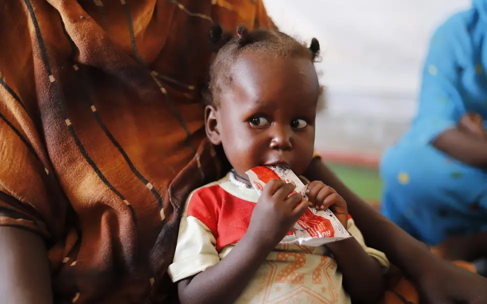Ein kleines Kind isst aus einer Packung Plumpy Nut