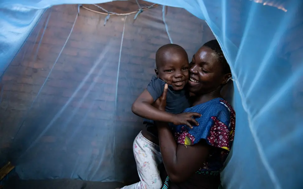 Malawi: Eine junge Mutter mit ihrem Sohn unter einem Moskitonetz I © UNICEF/UNI585037/Chikondi Die 20-jährige Mika hat von UNICEF Hilfsgüter erhalten. Das Moskitonetz schützt sie und ihren 4-jährigen Sohn vor Infektionen.