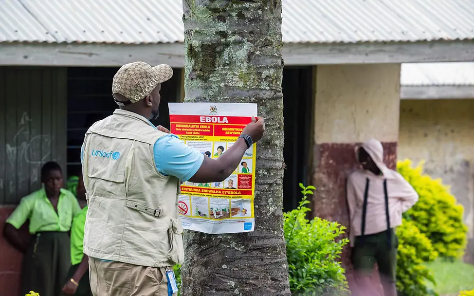 Ein UNICEF-Helfer hängt in Uganda ein Ebola-Aufklärungsposter an einen Baum | © UNICEF/Bamulanzeki Ebola-Bekämpfung: Ein UNICEF-Helfer hängt in Uganda ein Ebola-Aufklärungsposter an einen Baum