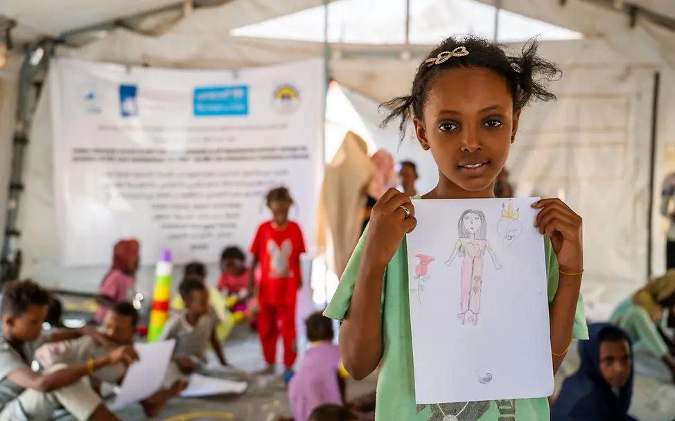 Ein geflüchtetes Mädchen zeigt stolz ihr selbstgemaltes Bild. | © UNICEF/Rajab Sudan Krieg: Ein geflüchtetes Mädchen hat in einem Spielzelt von UNICEF ein Bild gemalt und zeigt es stolz.