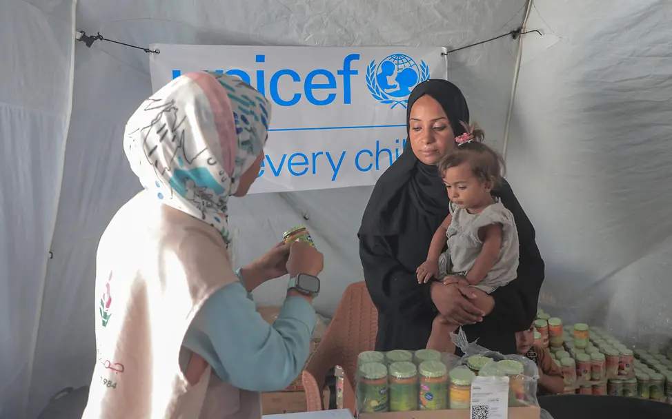 UNICEF hilft Menschen im Gazastreifen | © UNICEF/UNI856410/Nateel EIne UNICEF Mitarbeiterin gibt Babynahrung an eine Frau