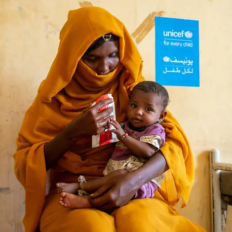 Eine Mutter hat ihr Kind auf dem Schoß und gibt ihm therapeutische Zusatznahrung