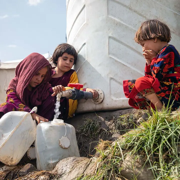 Kinder füllen Wasser aus einem großen UNICEF-Wassertank in ihre Kanister | © UNICEF/Azizi Afghanistan Nothilfe spenden: Kinder in einem Flüchtlingscamp füllen Wasser in Kanister ab.