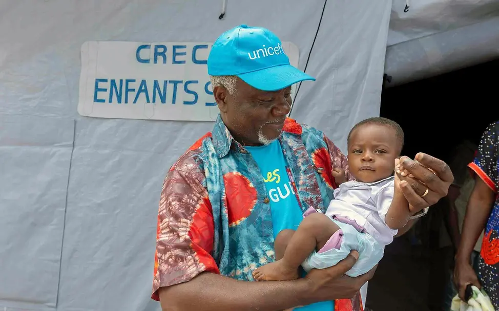 Ein UNICEF-Mitarbeiter hält ein Baby auf dem Arm. | © UNICEF/Badimu Ebola Kongo: Ein UNICEF-Kinderschutz-Mitarbeiter hält ein Baby in einer von UNICEF eingerichteten Kinderkrippe auf dem Arm.