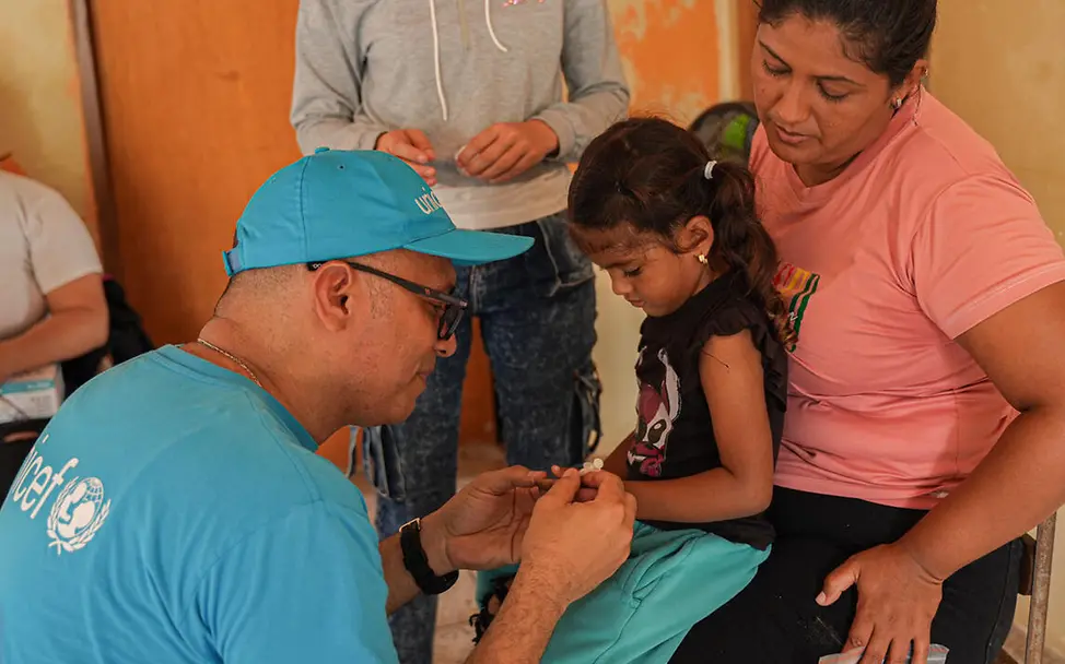 Ein UNICEF-Gesundheitshelfer in Venezuela versorgt ein auf dem Schoß ihrer Mutter sitzendes Mädchen. | © UNICEF/Pocaterra Venezuela Armut: Ein UNICEF-Gesundheitshelfer bereitet ein Mädchen auf seine Impfung vor.