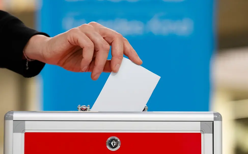 Was ist Demokratie einfach erklärt: Ein Wahlzettel wird in die Wahlurne geworfen. 