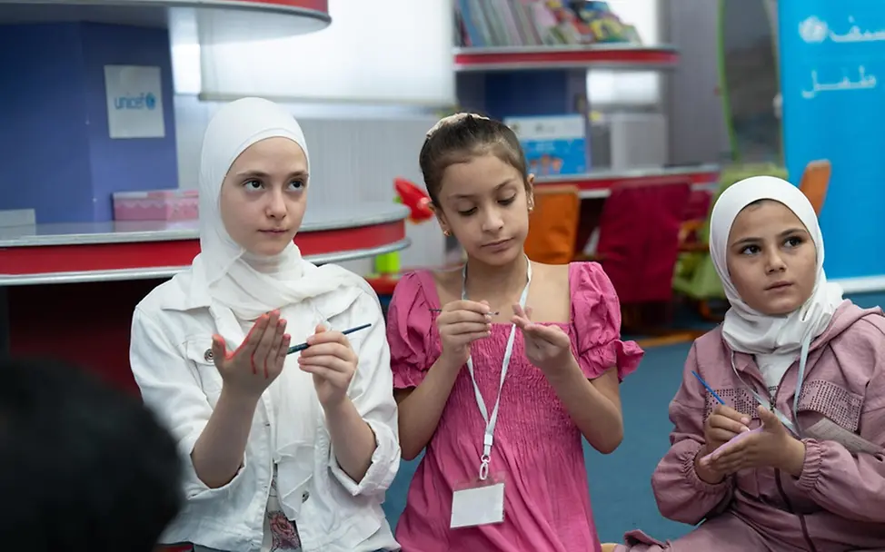 Elizabeth, Aline und Sham nehmen an einer Malaktion in einem kinderfreundlichen Zentrum in Syrien teil. 