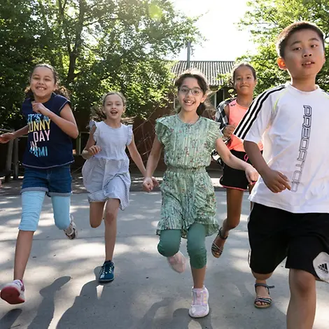 Menschenrechte einfach erklärt: Alle Menschen haben die gleichen Rechte, von Geburt an und ihr ganzes Leben lang. Menschenrechte einfach erklärt: Kinder laufen lachend auf einem Schulhof.