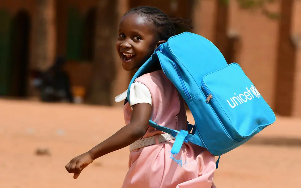Menschenrechte einfach erklärt: Bildung und Arbeit sind Menschenrechte – jedes Kind soll zur Schule gehen können. Menschenrechte einfach erklärt: Ein Mädchen mit einem UNICEF-Schulrucksack blickt lachend über die Schulter.