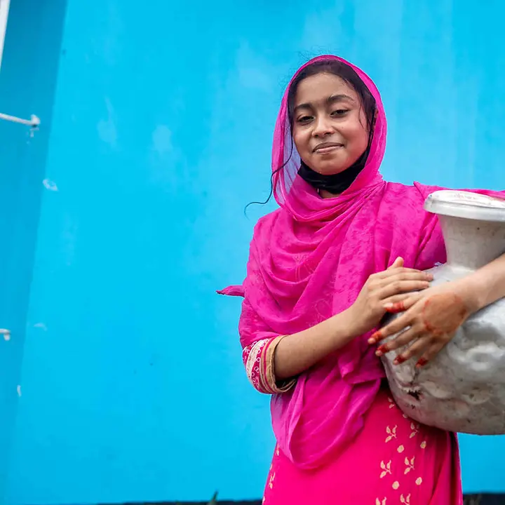 Arsen im Trinkwasser: Ein Mädchen mit einem Wassergefäß aus Metall lächelt in die Kamera.
