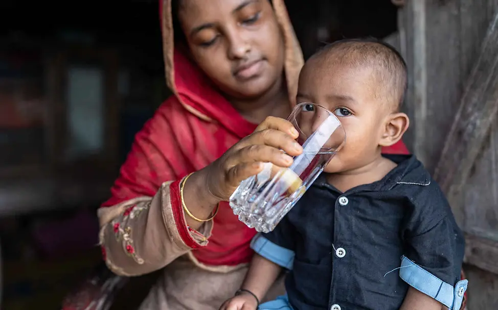 Arsen im Trinkwasser: Eine Mutter gibt ihrem Kind ein Glas sauberes Wasser zu trinken.