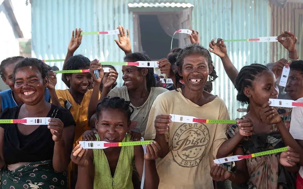Madagaskar Hungerkrise: Frauen halten lachend Testbänder für Mangelernährung in die Kamera.