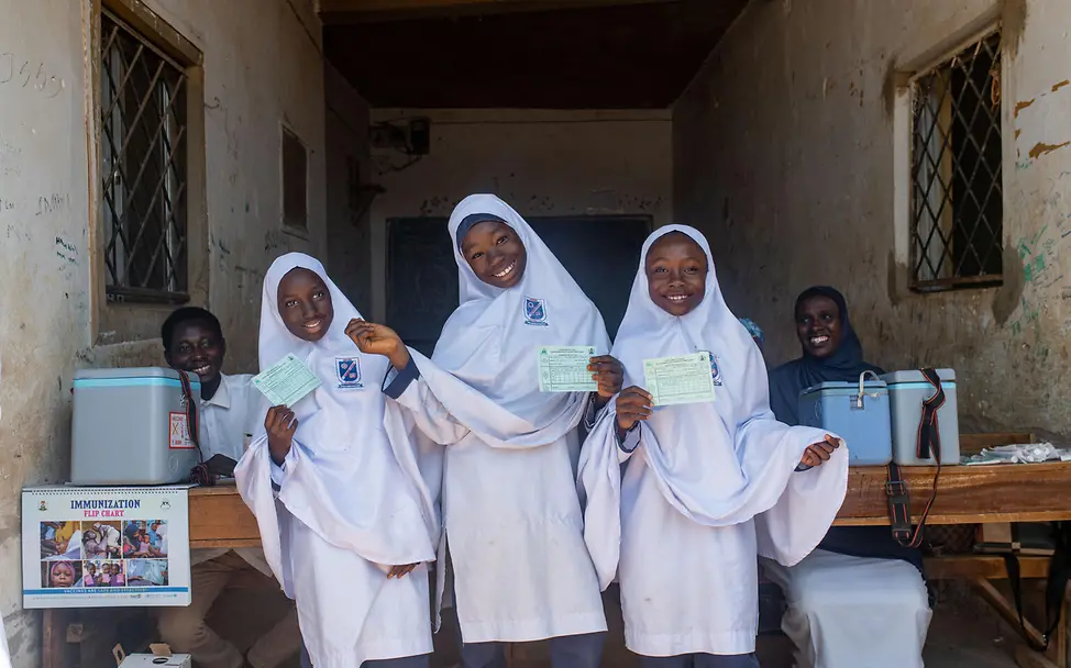 Gute Nachrichten aus Nigeria: Drei Mädchen stehen in ihrer Schule und lächeln nach Erhalt einer Impfung.