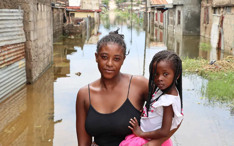 Was ist Klimaschutz: Heftige Regenfälle und Überschwemmungen werden durch den Klimawandel häufiger. | © UNICEF/Assane Klimaschutz einfach erklärt: Eine Mutter steht mit ihrer Tochter auf dem Arm in einer überschwemmten Straße.