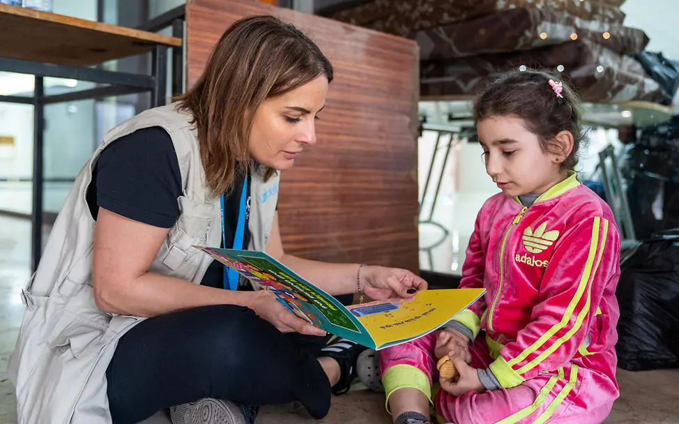 Libanon spenden: Eine UNICEF-Helferin schaut mit einem Mädchen in einer Notunterkunft ein Buch an 
