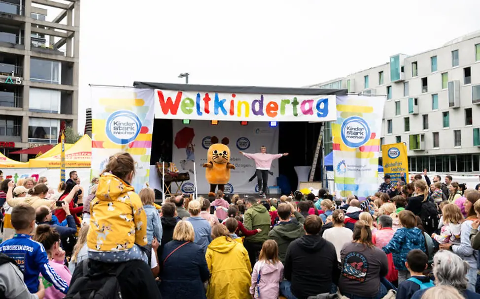 Weltkindertag Kindern erklären: In vielen Städten gibt es Feste und Demonstrationen zum Weltkindertag | © UNICEF/Etges Weltkindertag einfach erklärt: Die Maus vor vielen Kindern auf einer Bühne