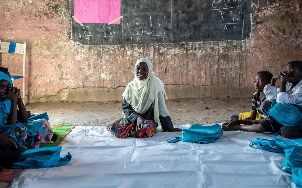 Kinder sitzen vor einer Tafel auf dem Boden