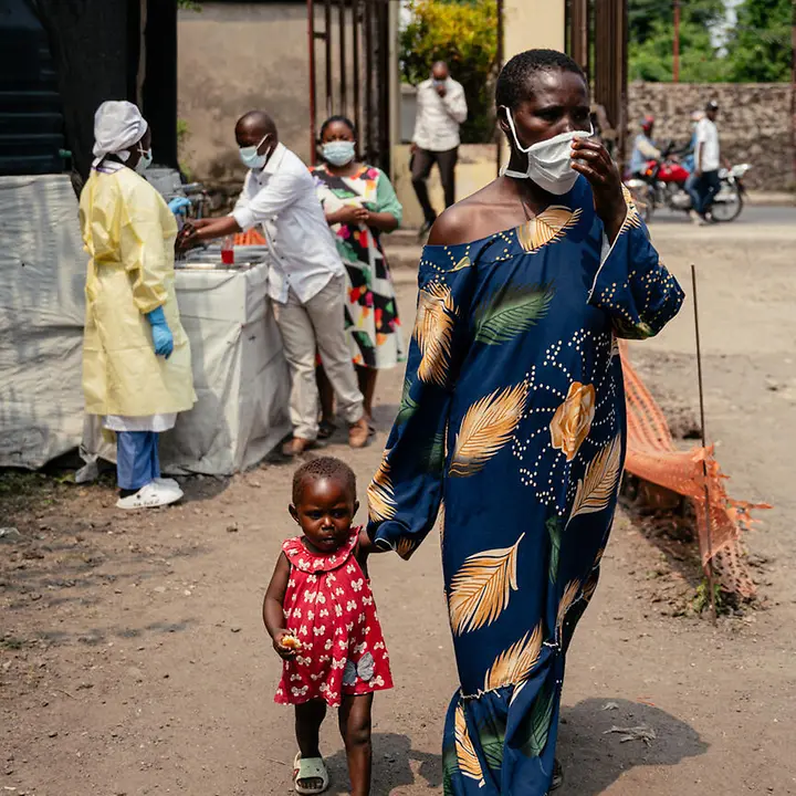 Ebola Kongo spenden: Eine Frau mit Atemschutzmaske geht mit ihrem Kind an der Hand an einer Gesundheitsstation im Kongo vorbei. 