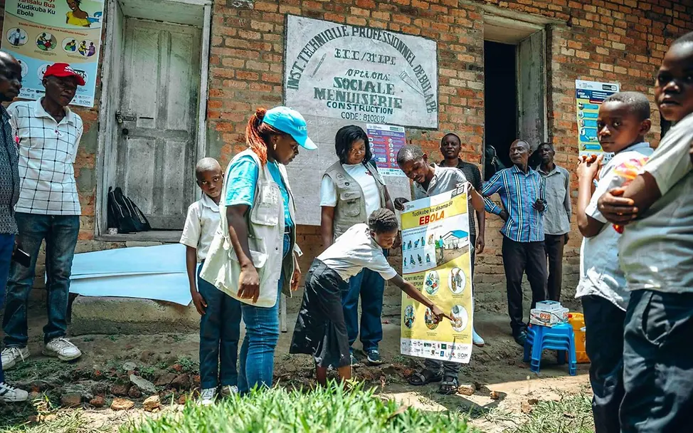 Eine UNICEF-Mitarbeiterin zeigt Kindern ein Poster mit Hygieneschutz-Maßnahmen gegen Ebola. | © UNICEF/Badimu Ebola Afrika: Eine UNICEF-Mitarbeiterin zeigt Kindern im Kongo, wie sie sich vor Ebola schützen können.