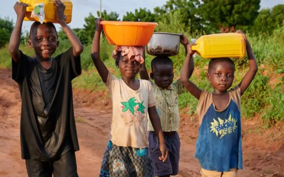 Vier Kinder tragen Wasserkanister auf dem Kopf | © UNICEF/UNI680192/Noorani Vier Kinder gehen auf einem roten Feldweg und tragen Kanister und eine Schüssel auf dem Kopf.